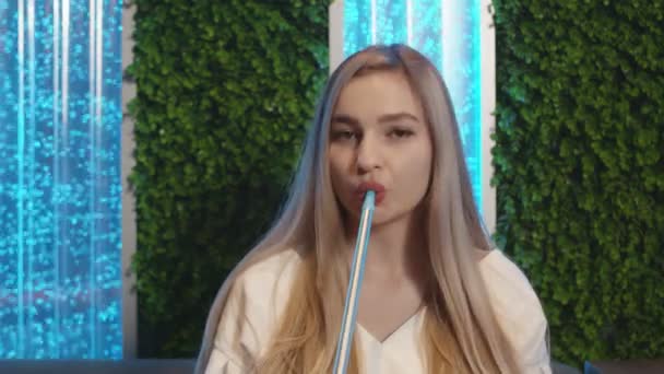 Fiatal szőke nő dohányzik vízipipa és néz a kamerába - Felvétel, videó