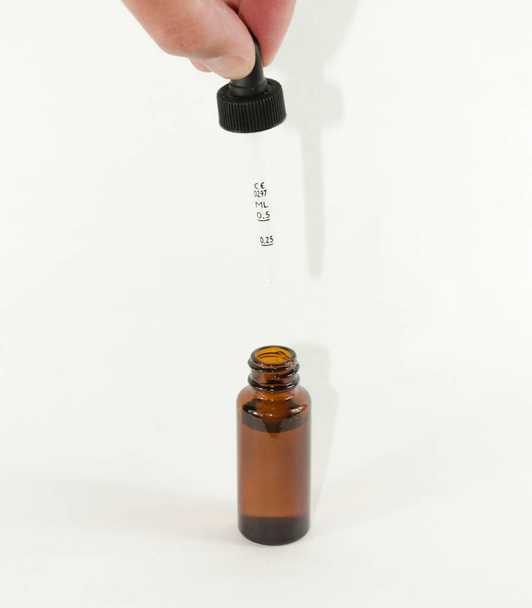 üveg palack cseppentővel egyik kezében, cseppentő izolált fehér alapon - Fotó, kép