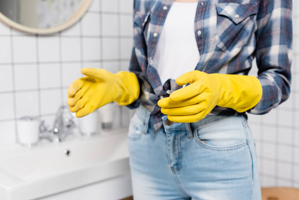 Cropped view of woman in rubber gloves standing in bathroom on blurred background - Valokuva, kuva