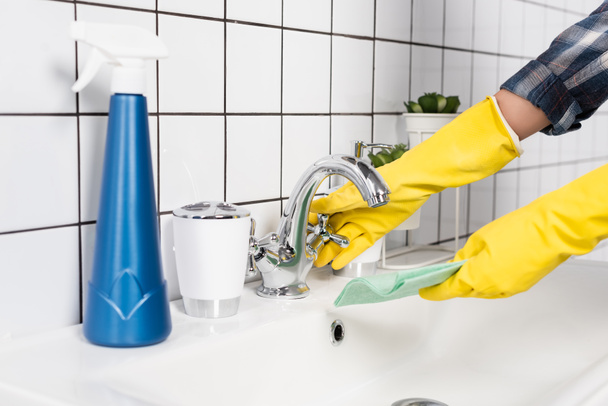 Cropped view of woman in rubber gloves wetting rag near detergent on blurred foreground in bathroom  - Valokuva, kuva
