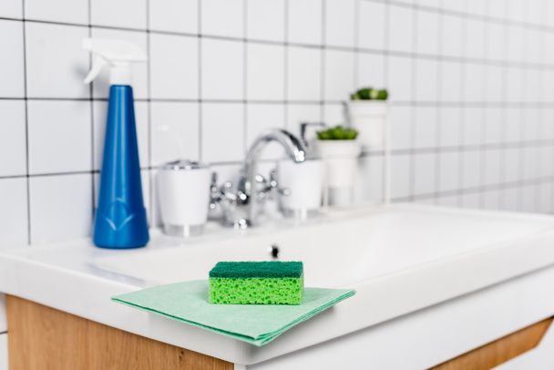 Губка на ганчірці біля миючого засобу на раковині у ванній на розмитому фоні
  - Фото, зображення