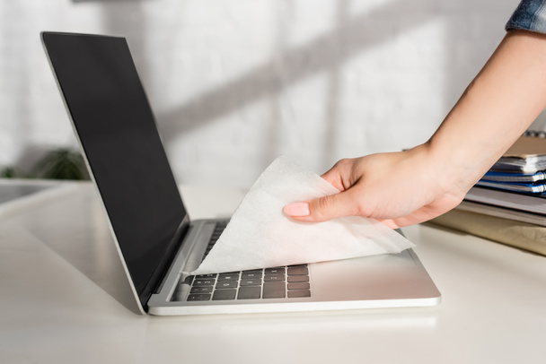 Обрізаний вид жіночої чистки клавіатури ноутбука з серветкою біля блокнотів на столі
  - Фото, зображення