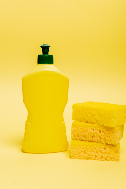 Губки и бутылка жидкости для мытья посуды на желтом фоне - Фото, изображение