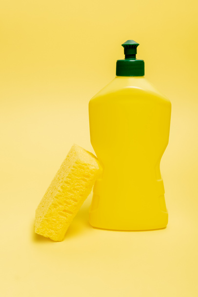 Esponja perto de garrafa de líquido de lavar louça no fundo amarelo com espaço de cópia  - Foto, Imagem