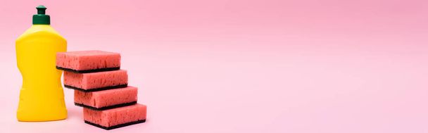 Bottle of dishwashing liquid and sponges on pink background, banner  - Zdjęcie, obraz