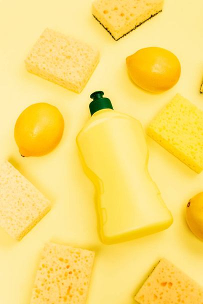 Top view of dishwashing liquid, sponges and lemons on yellow background - 写真・画像