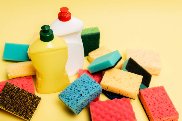 High angle view of dishwashing liquid and sponges on yellow background - Фото, изображение