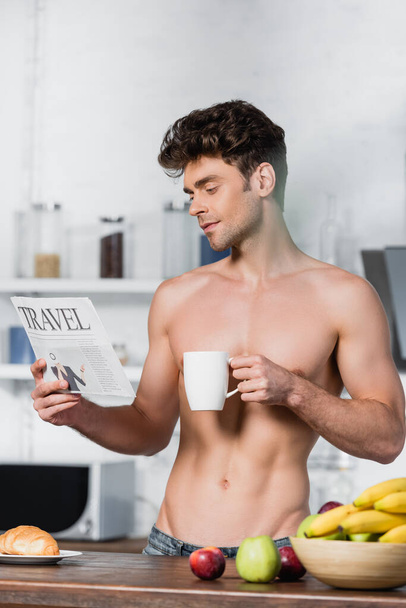 Izmos férfi olvasás utazási hírek és holding csésze reggeli közben a konyhában  - Fotó, kép