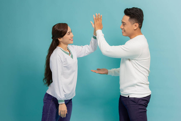 Image of friendly young people man and woman in basic clothing laughing and giving high five isolated over blue background - Fotó, kép