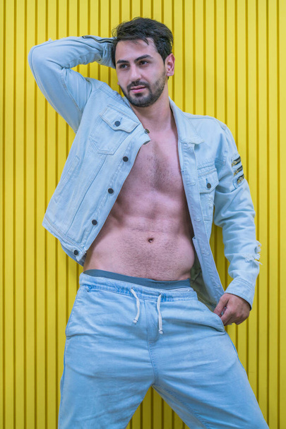 portrait of caucasian strong man model posing in jean with yellow wall background - Photo, image