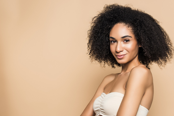 pretty african american woman with bare shoulders looking at camera isolated on beige  - Photo, image