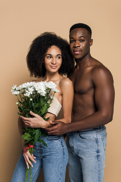 bez košile africký Američan muž objímající veselou ženu s květinami na béžové - Fotografie, Obrázek