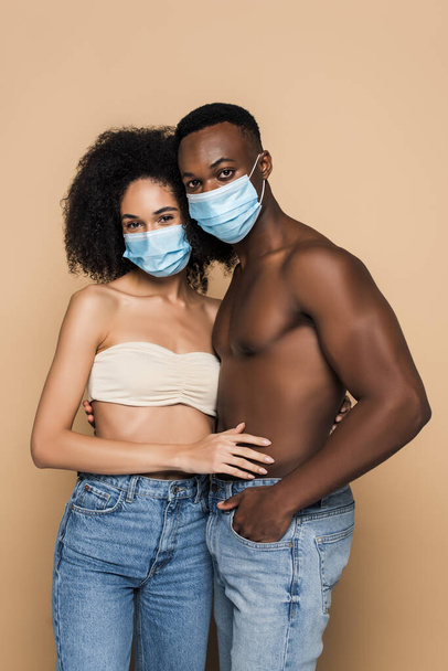 Afrikanisches Paar in medizinischen Masken blickt isoliert auf beige Kamera  - Foto, Bild