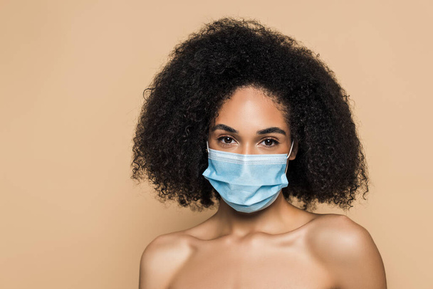 göndör afro-amerikai nő orvosi maszk csupasz vállak nézi kamera elszigetelt bézs  - Fotó, kép