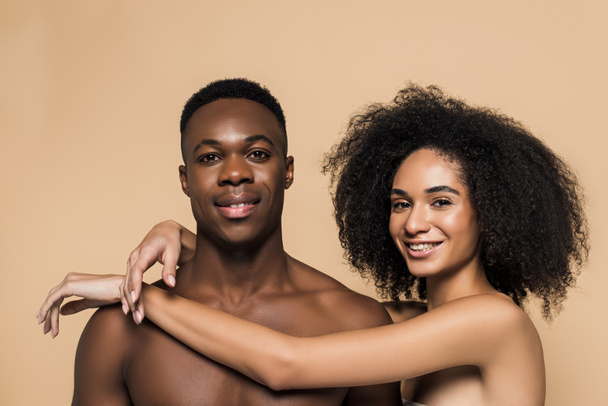 curly african american woman with bare shoulders hugging cheerful boyfriend isolated on beige  - Fotó, kép