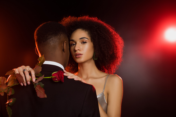 elegáns afro-amerikai nő gazdaság rózsa és ölelkező férfi formális viselet fekete - Fotó, kép