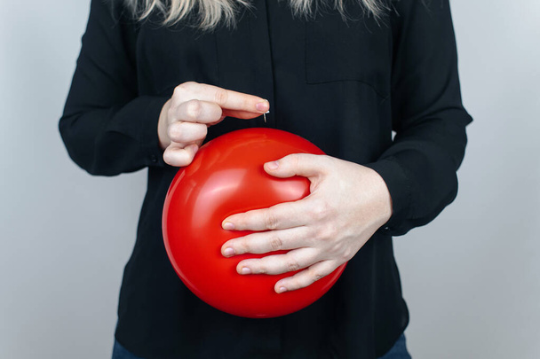 Fotografia konceptualna. Kobieta trzyma czerwoną kulę w pobliżu brzucha, co symbolizuje wzdęcia i wzdęcia. Potem wbija igłę, żeby rozerwać balon i pozbyć się problemu.. - Zdjęcie, obraz