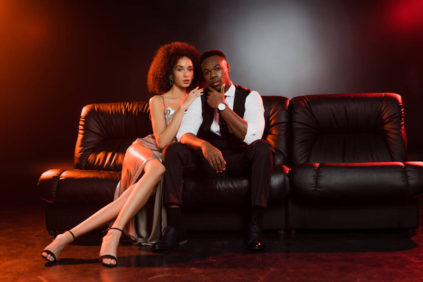 elegante coppia afroamericana seduta su divano in pelle su nero - Foto, immagini
