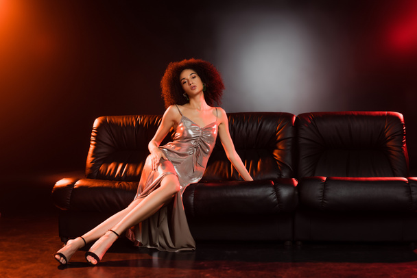 full length of elegant woman in dress sitting on couch on black background  - Foto, immagini