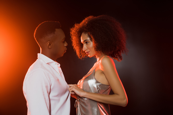 side view of curly african american woman undressing man on black  - Фото, зображення