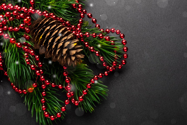 branch of a Christmas tree and a pine cone with decorations on a black background with a place for the text. Copy space - Photo, Image