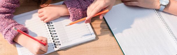 机の上にノートを書いている娘の近くの鉛筆で指摘する母親の作物のビュー、バナー - 写真・画像