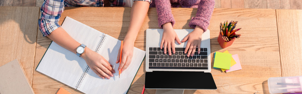 Обрізаний вид дочки, що друкує на ноутбуці біля матері за столом з канцелярськими приладами, банер
 - Фото, зображення