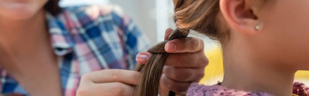 Cropped view of mother plaiting hair of daughter on blurred background, banner - Fotó, kép