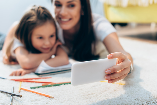 Cheerful mother and daughter taking selfie on floor on blurred background - Foto, immagini