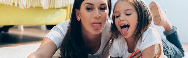 Happy mother and daughter with sticking out tongues looking down on floor on blurred background, banner - Фото, зображення