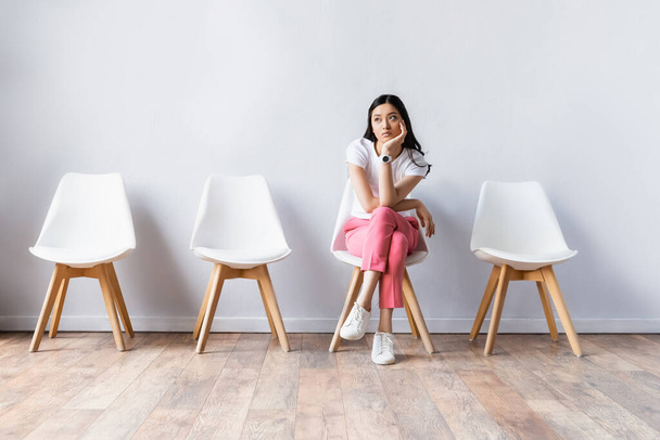 Bruna donna asiatica seduta sulla sedia mentre aspetta in sala  - Foto, immagini