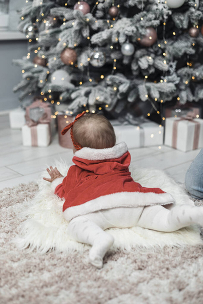 The baby kid at the Christmas tree waiting for Santa. A child looks at a huge Christmas tree and lights. First new year. - Foto, Imagen