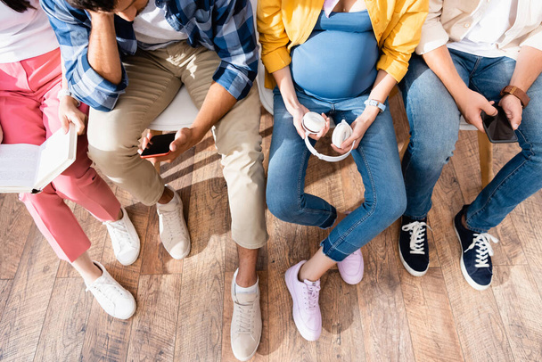 Top widok mężczyzny za pomocą smartfona w pobliżu kobiety w ciąży i ludzi w kolejce  - Zdjęcie, obraz