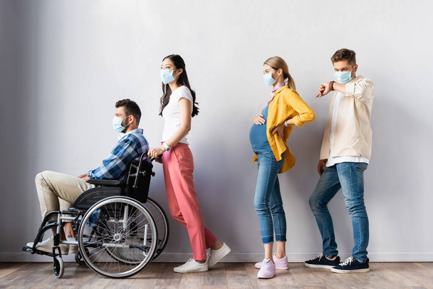 Multiethnic people in medical mask standing near disabled man and pregnant woman in hall  - Photo, Image