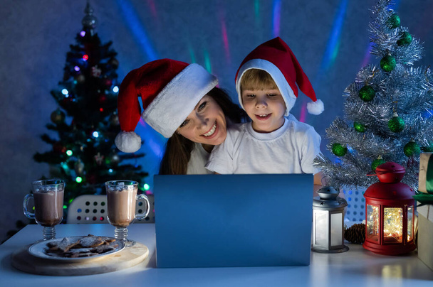 Happy mom and son talking on a video call on a laptop on christmas night. - Photo, image