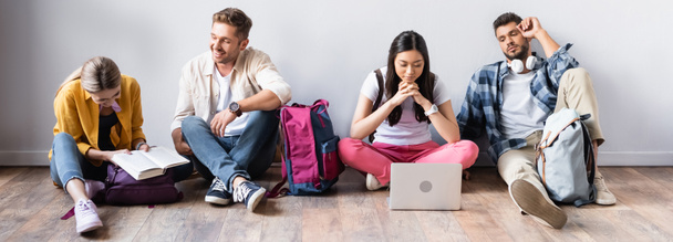 Estudantes multiétnicos com laptop, livro e mochilas sentadas no chão, banner  - Foto, Imagem