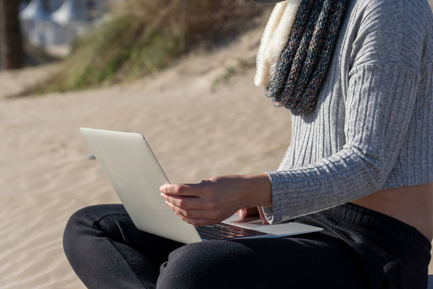 A shallow focus shot of a female with a laptop on a beach in Spain - 写真・画像