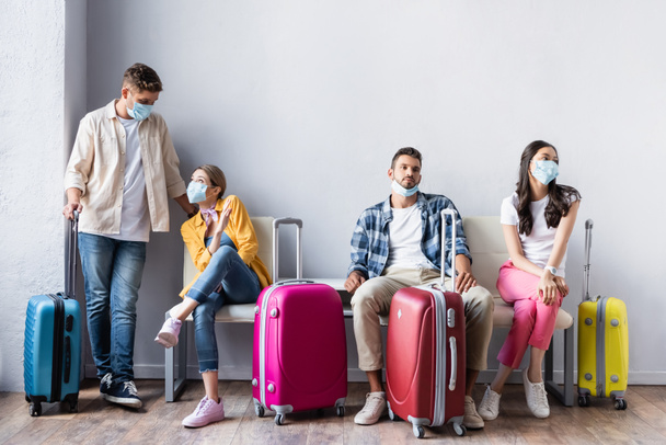 Мультикультурные люди в медицинских масках ждут возле чемоданов в аэропорту  - Фото, изображение