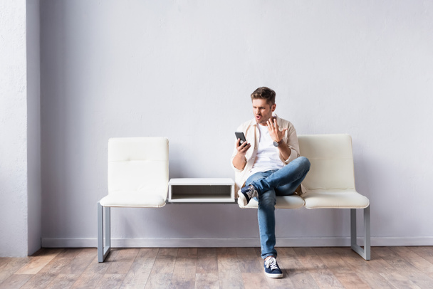 Aggressive man using smartphone while sitting on chair in hall  - Foto, immagini