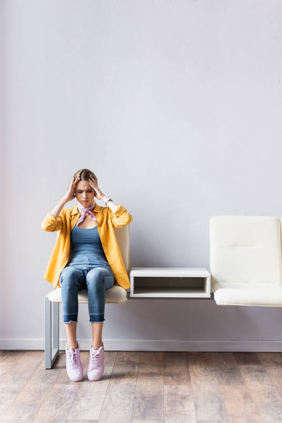 Женщина страдает от головной боли во время ожидания на стуле в холле  - Фото, изображение