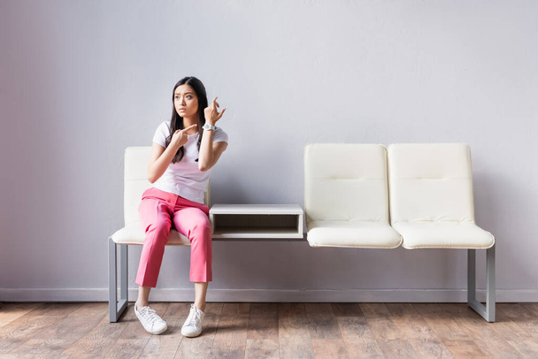 aziatische vrouw wijzend met vinger naar polshorloge op stoelen  - Foto, afbeelding