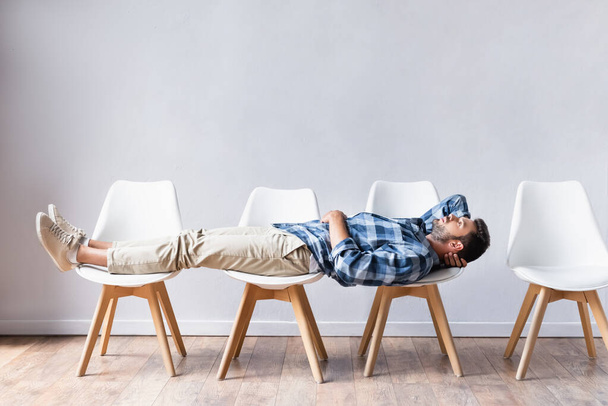 Man in casual wear lying on chairs while waiting in hall  - Photo, Image