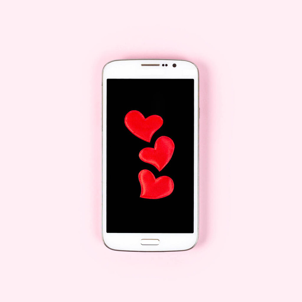 Teléfono móvil con pantalla negra y corazón rojo aislado sobre fondo rosa pastel. Vista superior, plano, espacio de copia. Día de San Valentín, amor, tecnología, concepto de citas en línea. - Foto, imagen
