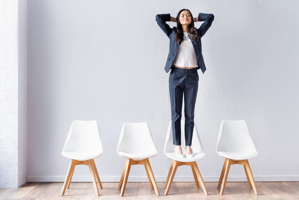 Asian businesswoman standing with closed eyes on chair in office  - Foto, Imagen