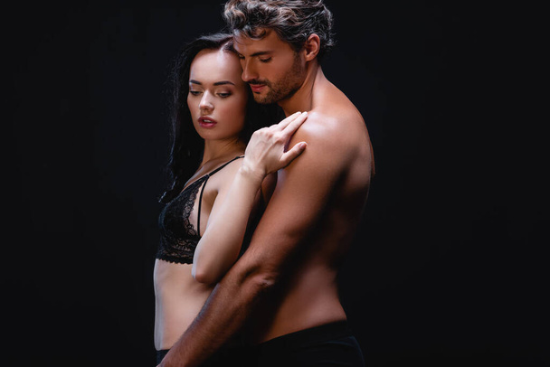 mladý bez košile muž objímání sexy žena v krajka podprsenka izolované na černé - Fotografie, Obrázek