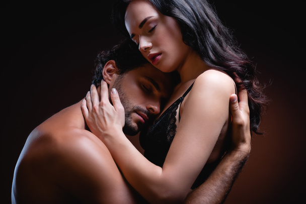 χωρίς πουκάμισο άντρας αγκαλιάζει σέξι γυναίκα με μαύρη δαντέλα σουτιέν σε σκούρο φόντο - Φωτογραφία, εικόνα