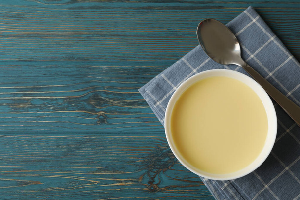 Towel, spoon and bowl with condensed milk on wooden background - Photo, image