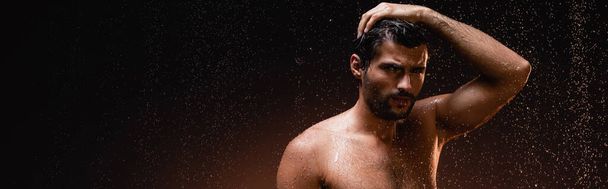sexy bez koszulki mężczyzna w deszczu patrząc w aparat na ciemnym tle, sztandar - Zdjęcie, obraz
