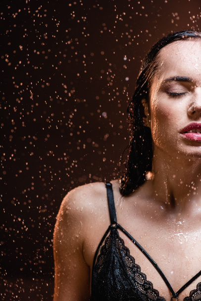 Siyah dantelli sütyenli şehvetli kadın, koyu arkaplanda yağan yağmurun altında gözleri kapalı. - Fotoğraf, Görsel