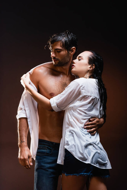seductive woman taking off wet shirt from sexy man on dark background - Photo, Image